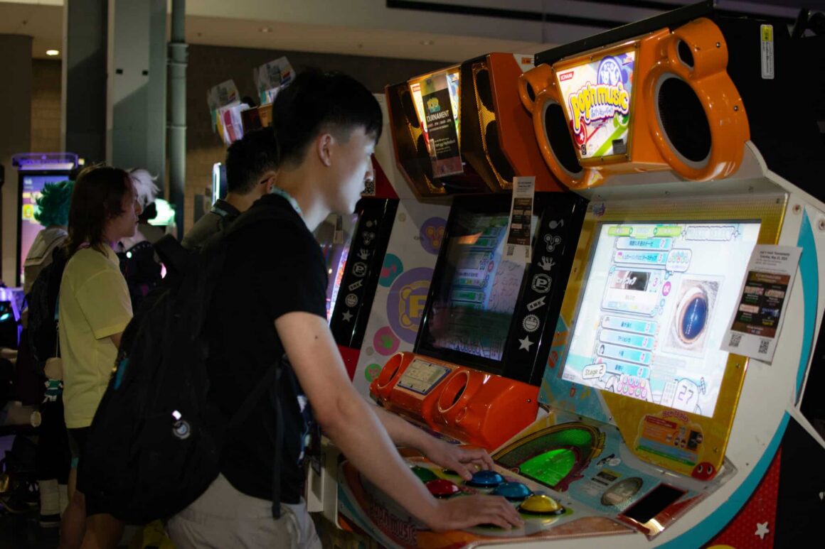 Young  adults are standing at at large gaming consoles, playing games at MomoCon2025.