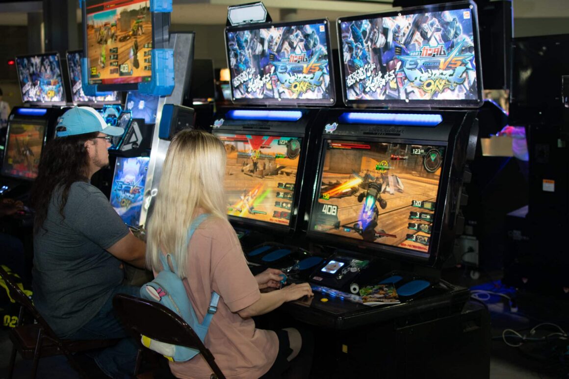 Young adults are sitting at gaming cabinet consoles, playing games at MomoCon 2025.