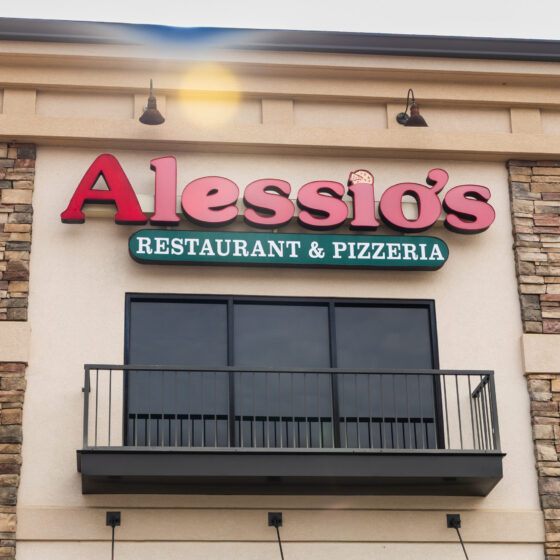 Exterior of tan-colored building with a large Alessio's Restaurant & Pizzeria sign.