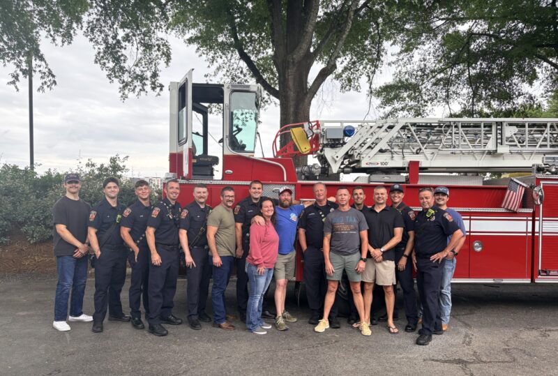A group of people standing together in front of a fire truck at a fundraising event.