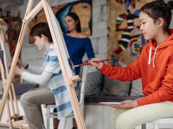 Two students sitting at easels with the teacher in the background in an art class.