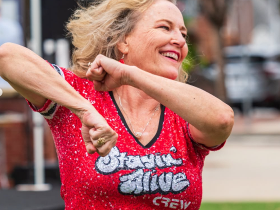 An older woman in a red shirt with the words 'stayin' alive' on the front is outside, exercising and smiling.